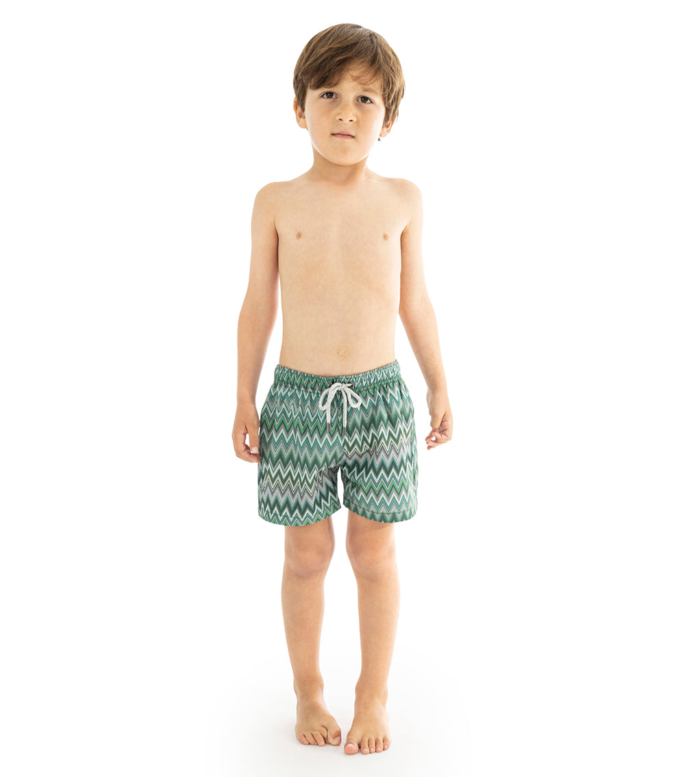 Chevron Young boy wearing green zigzag patterned swim shorts on a white background