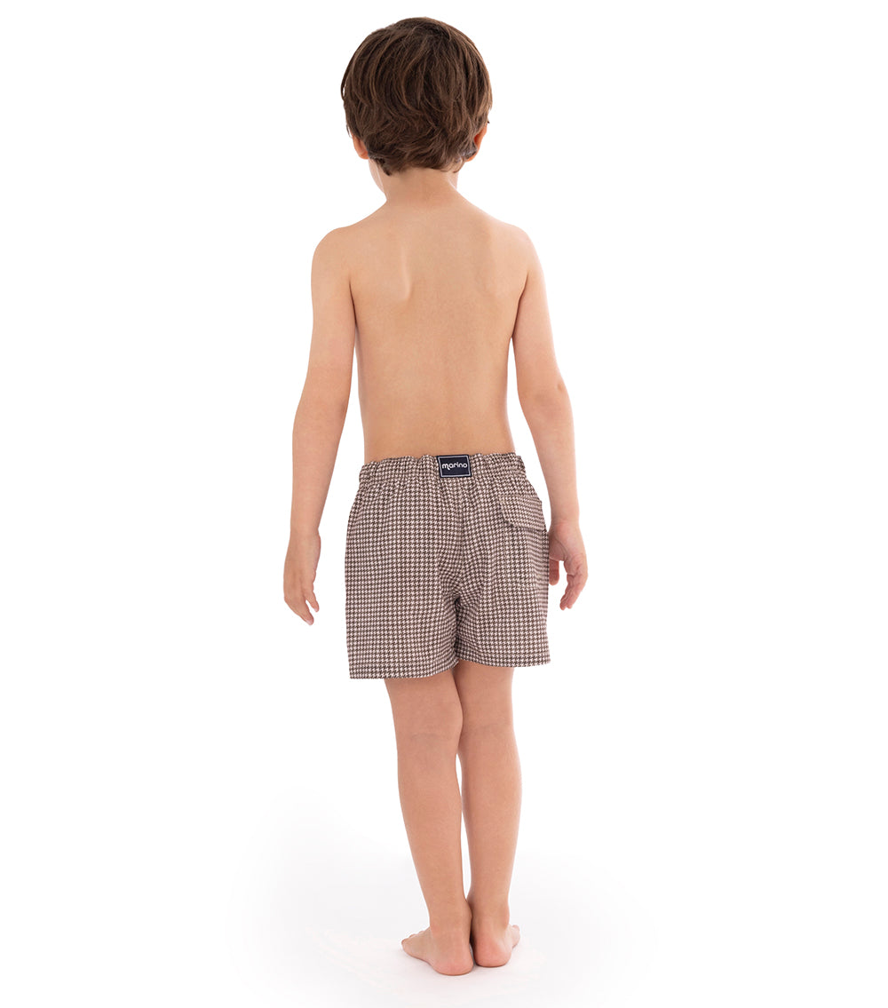 Houndstooth Young boy wearing brown printed swim shorts on a white background