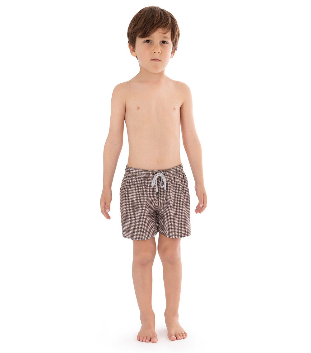 Houndstooth Young boy wearing brown printed swim shorts on a white background