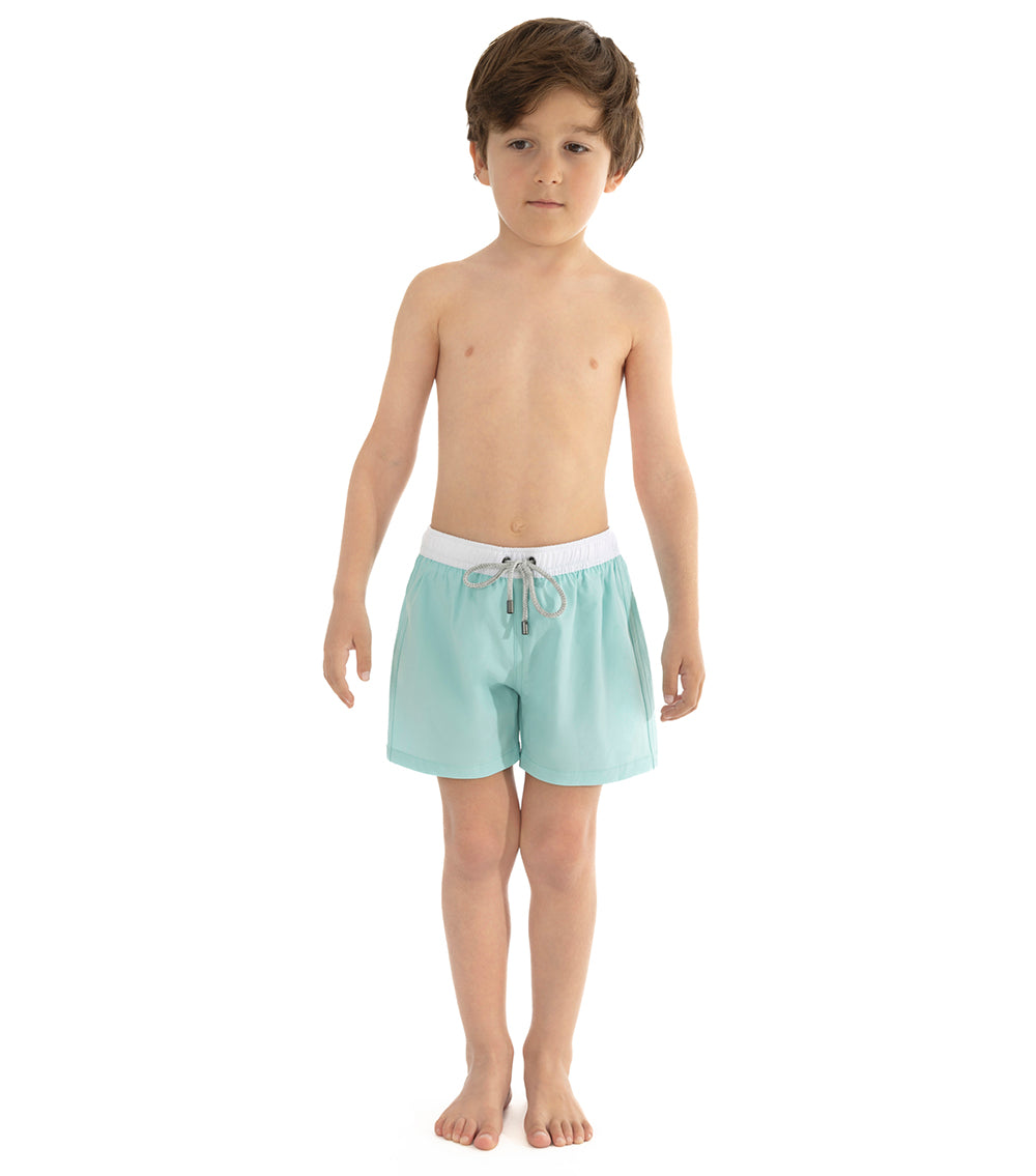 Aqua Young boy wearing light blue aquamarine swim shorts on a white background