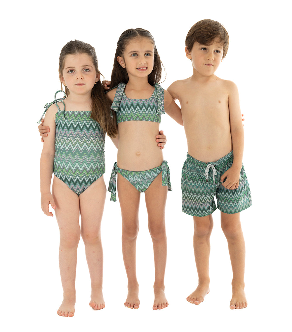 Chevron Three children wearing green zigzag patterned swimwear on a white background
