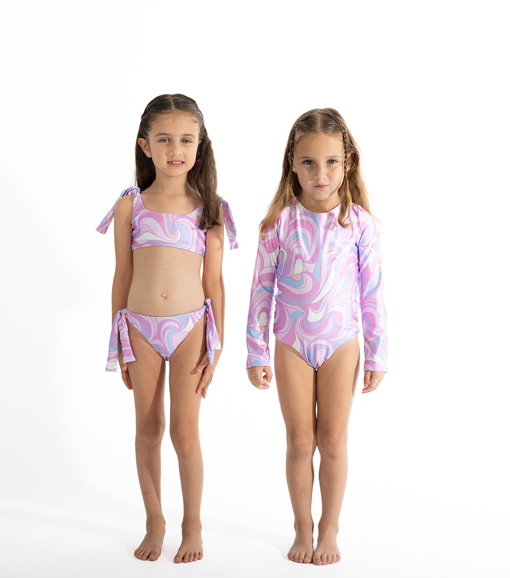 Groovy Two young girls wearing matching pink and purple swimsuits on a white background