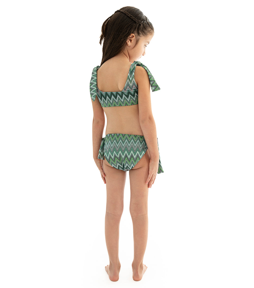 Chevron Young girl wearing a green and gray zigzag patterned two-piece swimsuit on a white background