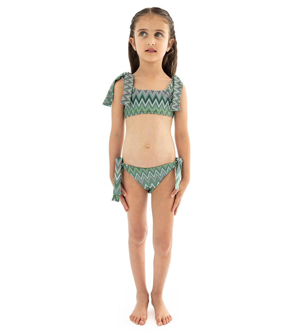 Chevron Young girl wearing a green and gray zigzag patterned two-piece swimsuit on a white background