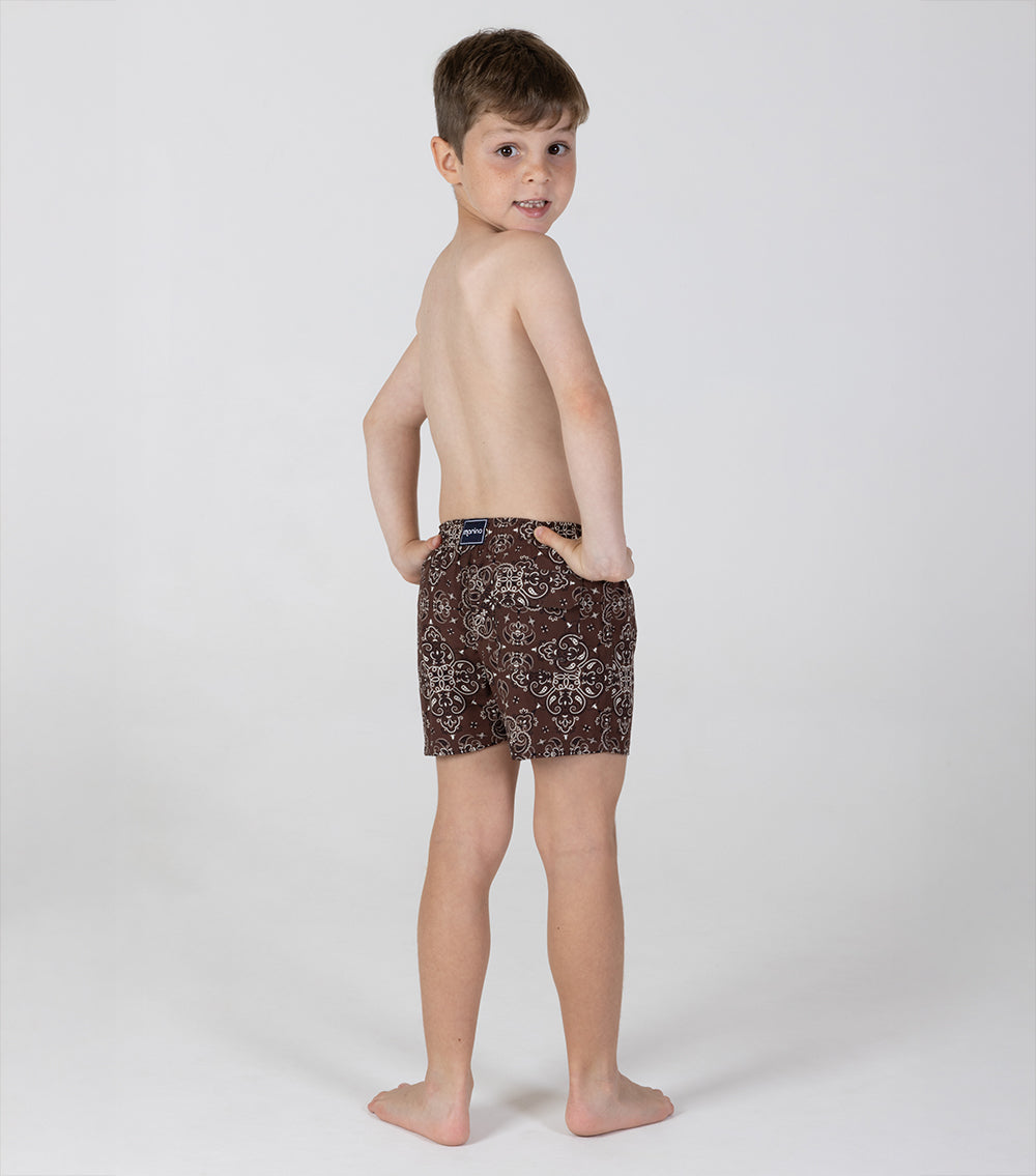 brown bandana Young boy wearing patterned swim shorts on a white background