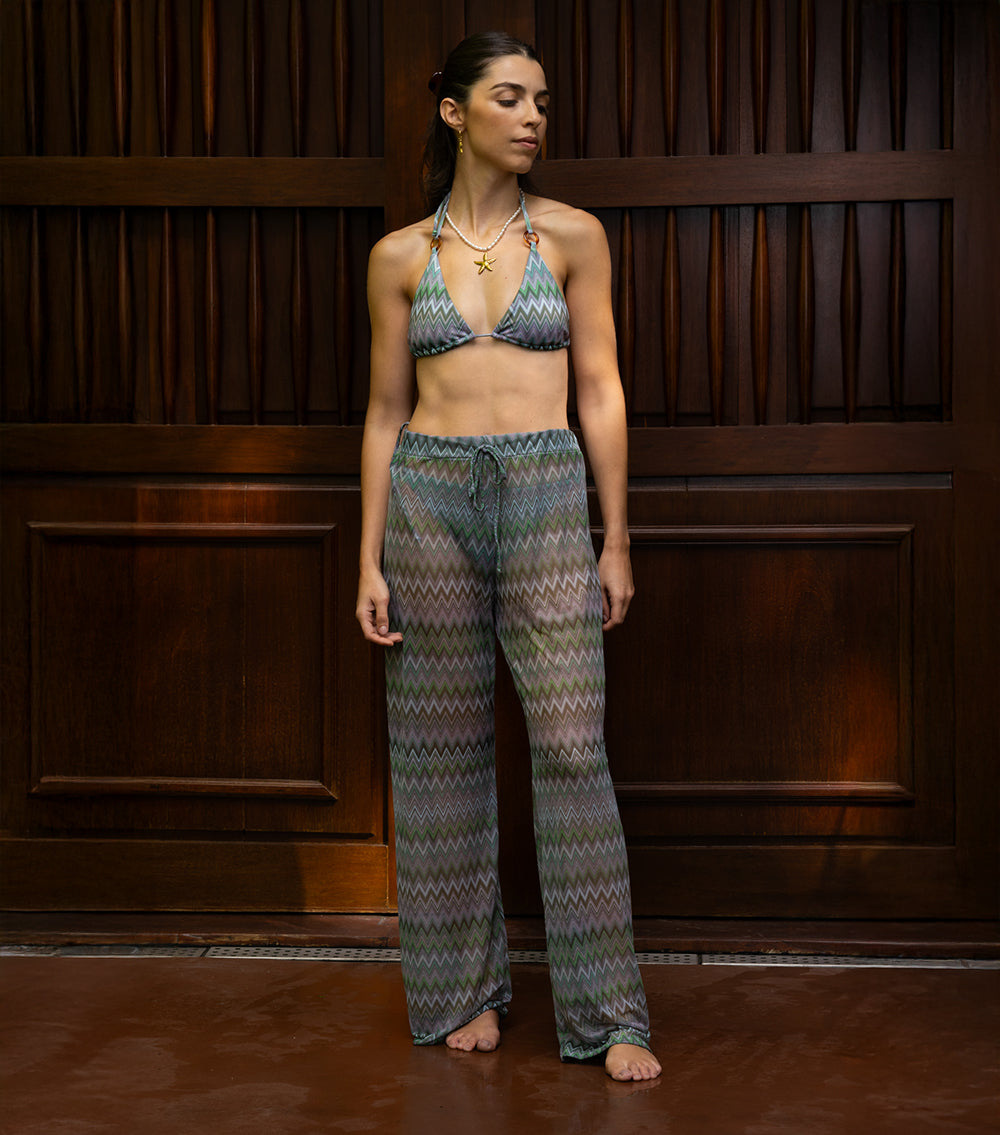 chevron Woman wearing a patterned bikini and pants against a wooden paneled wall.
