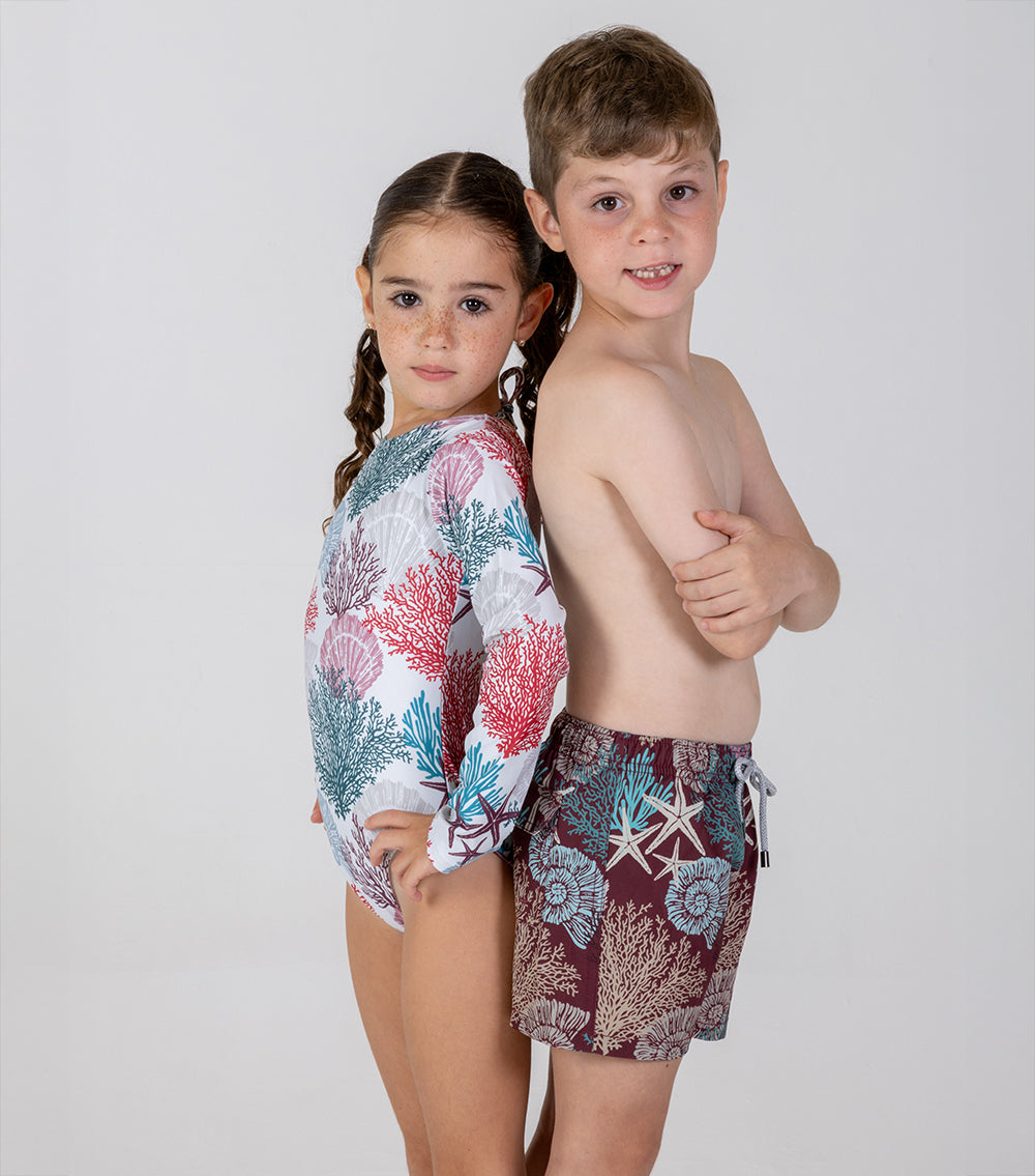 burgundy corals white corals Two children wearing colorful swimwear with floral and marine patterns on a white background