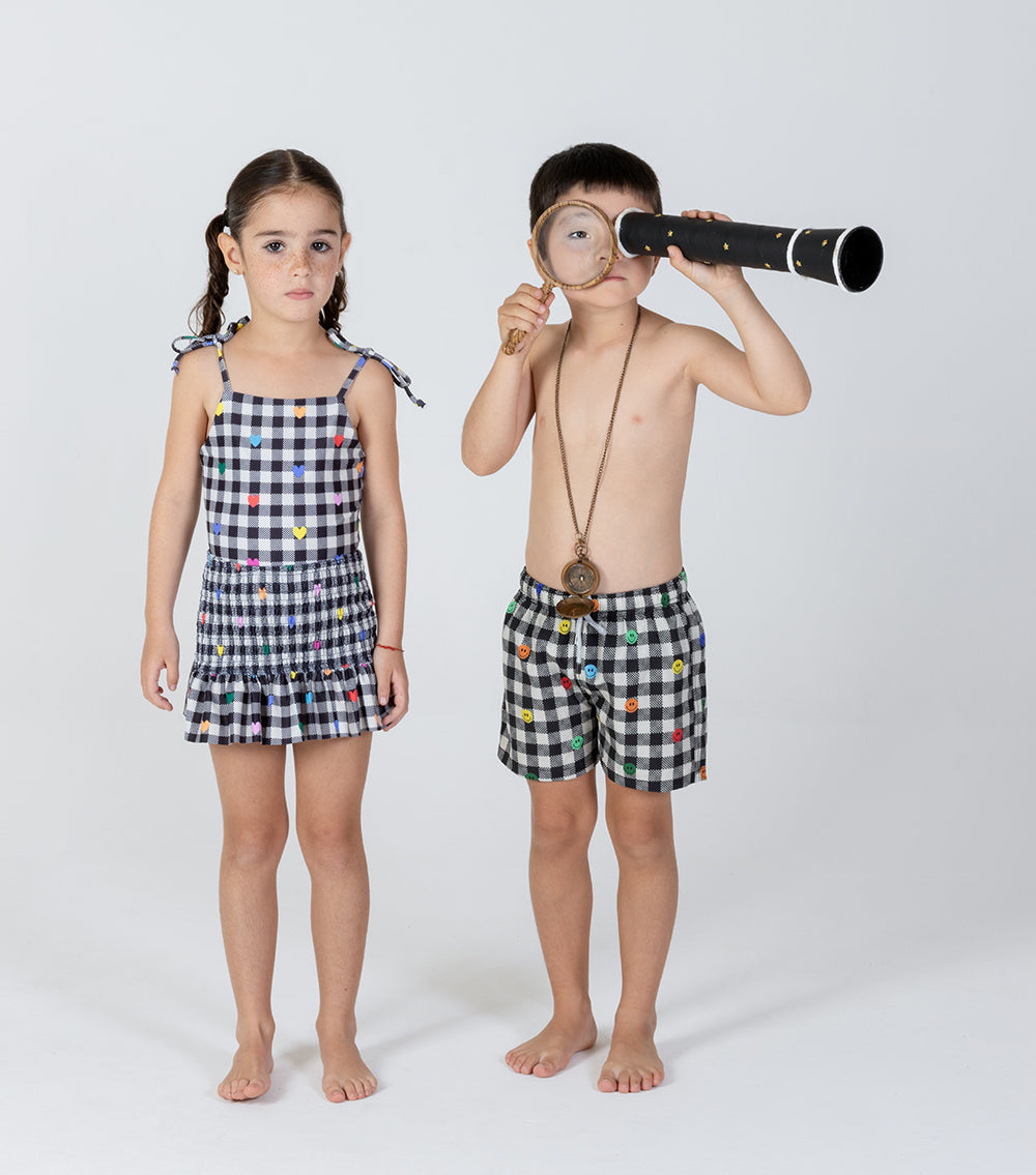 gingham emoji Two children in matching checkered outfits with a girl in a dress and a boy with a magnifying glass and telescope on a white background.