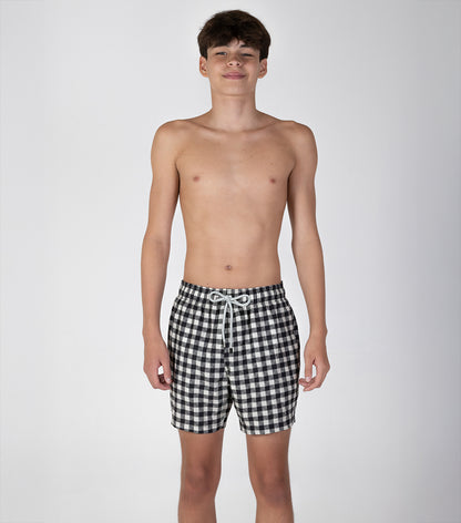 gingham Young boy wearing black and white checkered shorts on a plain background