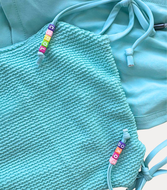 aqua textured top with colorful beaded straps on a matching turquoise background
